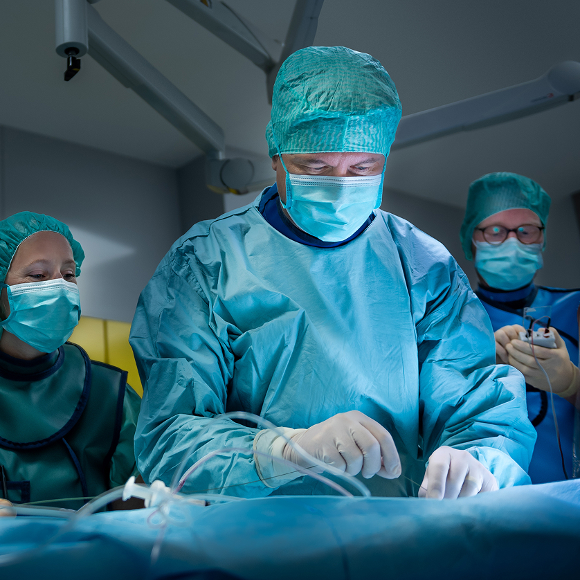 Prof. Dr. Benjamin Meder in OP-Kleidung beugt sich über einen Patienten. Im Hintergrund sind weitere Mitglieder des OP-Teams zu sehen.