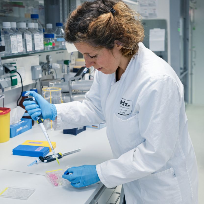 Eine Person im weißen Kittel und mit Handschuhen arbeitet mit einer Pipette.