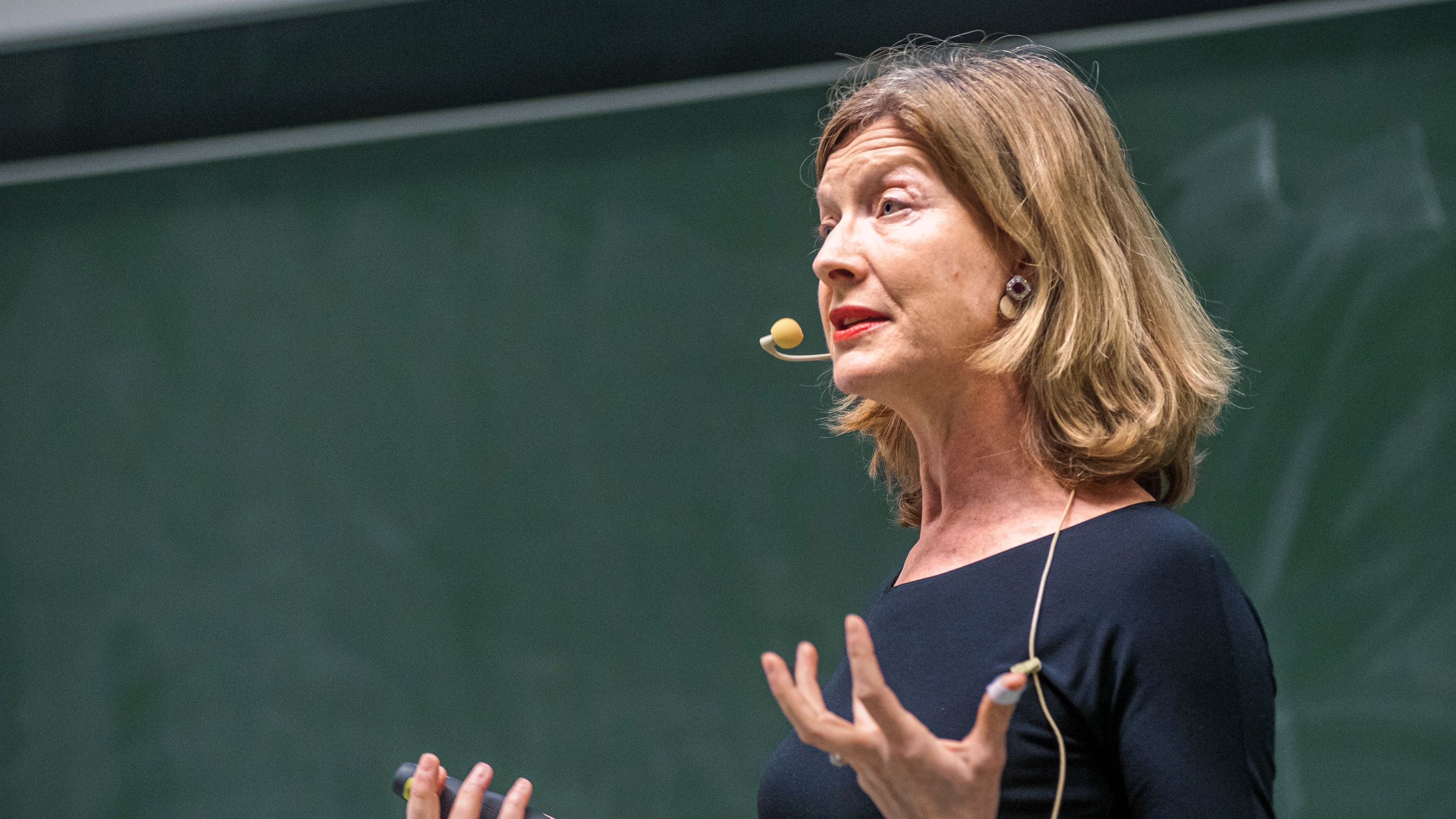 Prof. Dr. Hannah Monyer spricht mit Mikrofon vor einer Tafel – eine Vortragssituation.