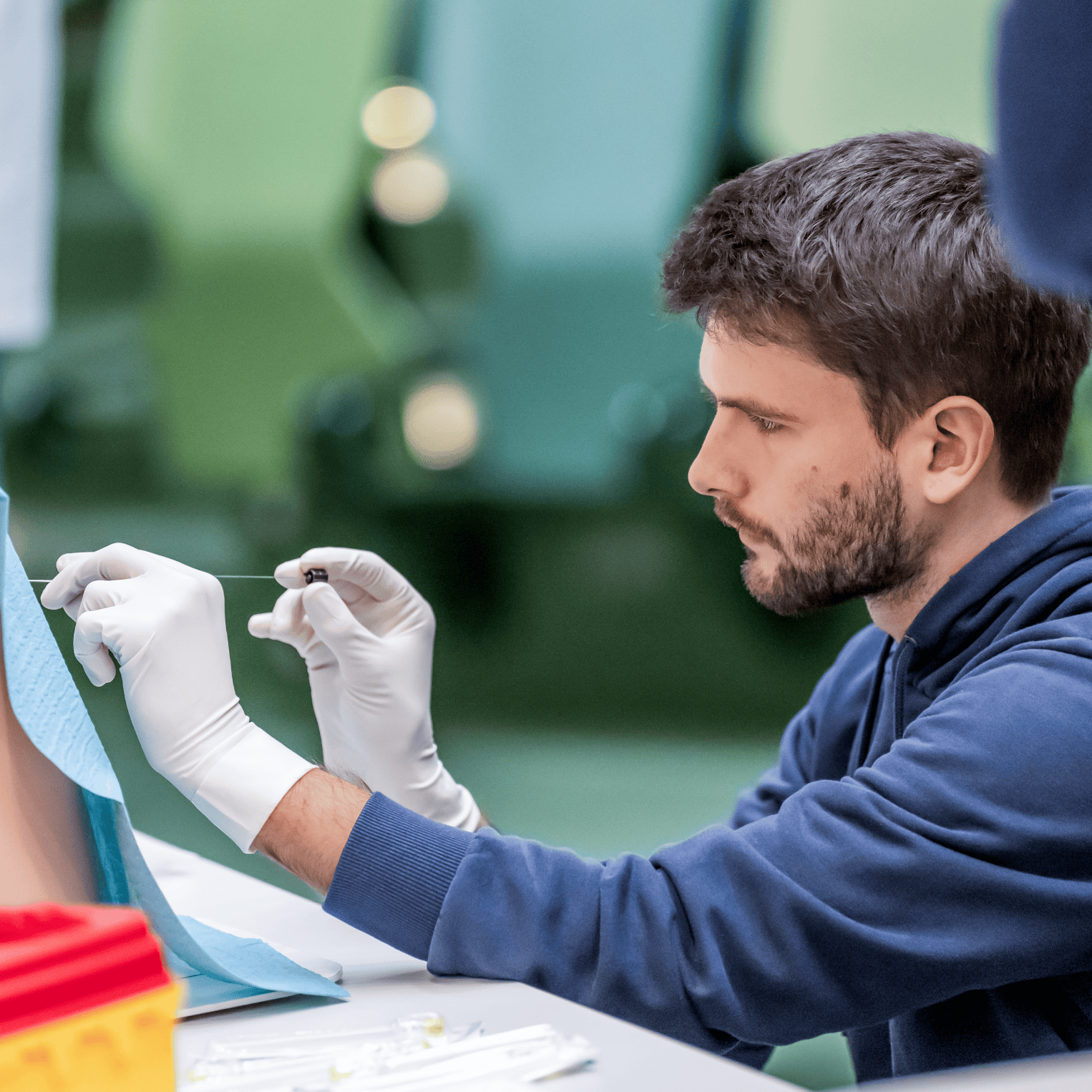 Übungssituation im Skills Lab: Ein junger Mann mit weißen Handschuhen hält eine lange Nadel an ein Modell eines menschlichen Rückens.