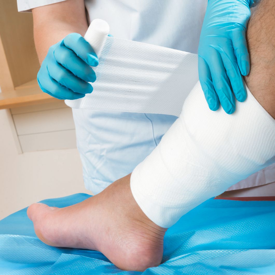 Hände legen einen Verband um einen Unterschenkel.