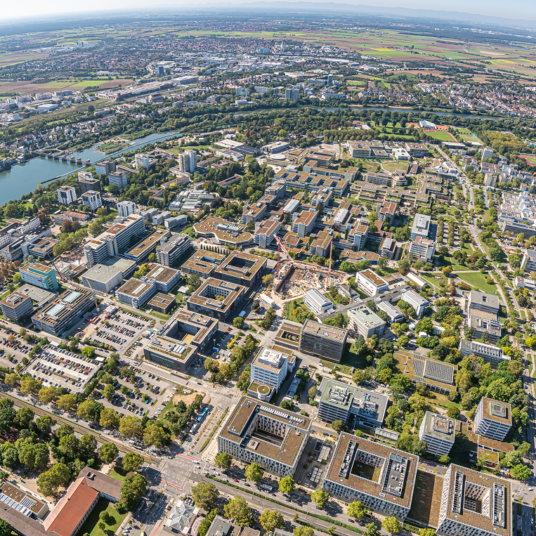 Luftbild des Neuenheimer Felds mit Klinik- und Universitätsgebäuden; im Hintergrund der Neckar